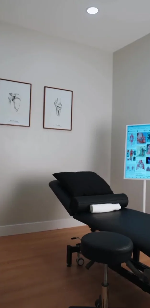 A private treatment room with a treatment table, stool and framed anatomy studies