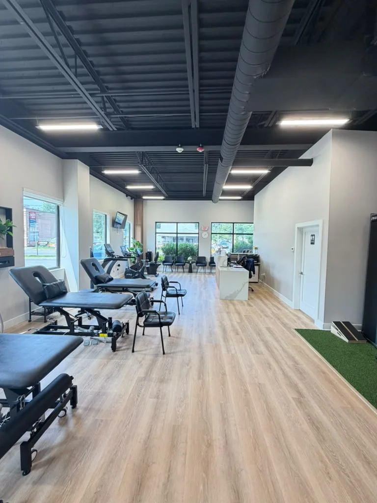 Treatment tables and chairs beneath a row of tall windows, with the front desk at the far end of the room